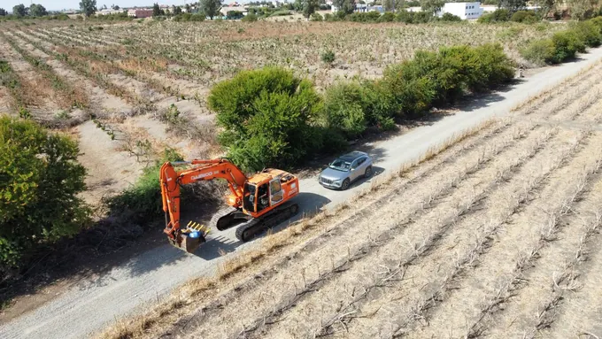 Excavatrice orange sur une piste bordant une exploitation agricole